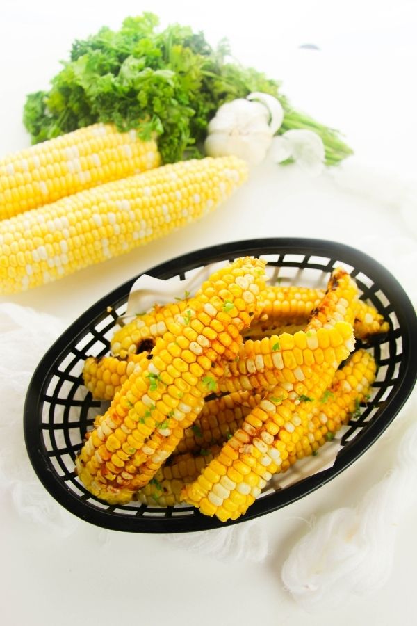 basket with corn on the cob inside it and corn in the background 